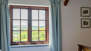 A room with a large window, curtains, and two framed pictures on the wall.