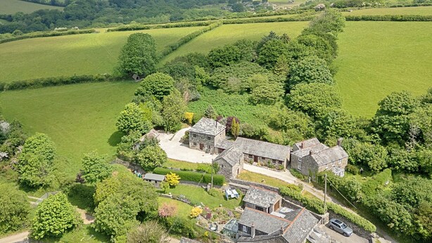 A rural property with stone buildings, a driveway, and surrounding green fields.
