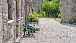 A stone building with a gravel path, a green metal table and chairs, and a potted plant.