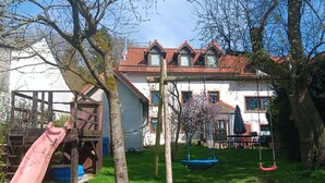 A backyard with a wooden slide, a swing set, and a house with a red-tiled roof.
