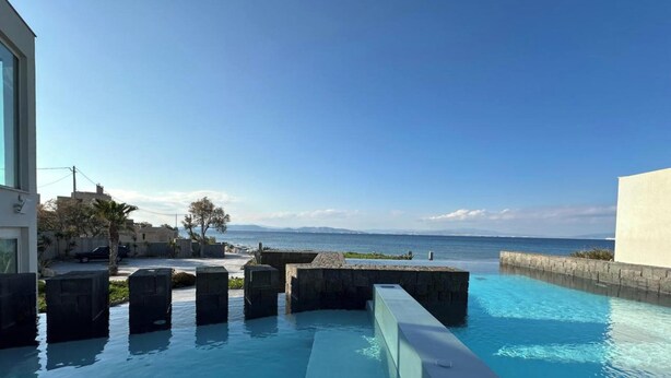 Una piscina con vistas claras al mar, un muro de piedra y un edificio moderno.