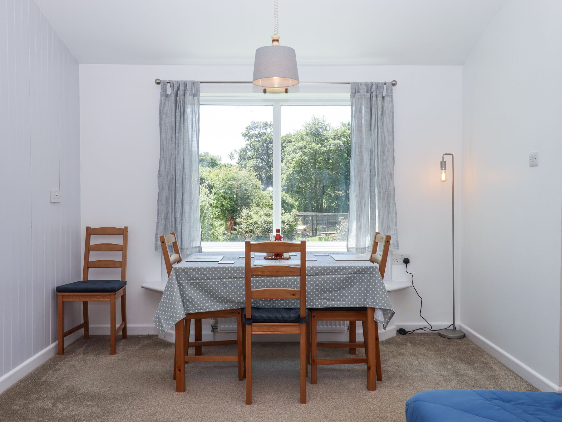A dining area with a table set for two, a chair, a floor lamp, and a window with curtains.