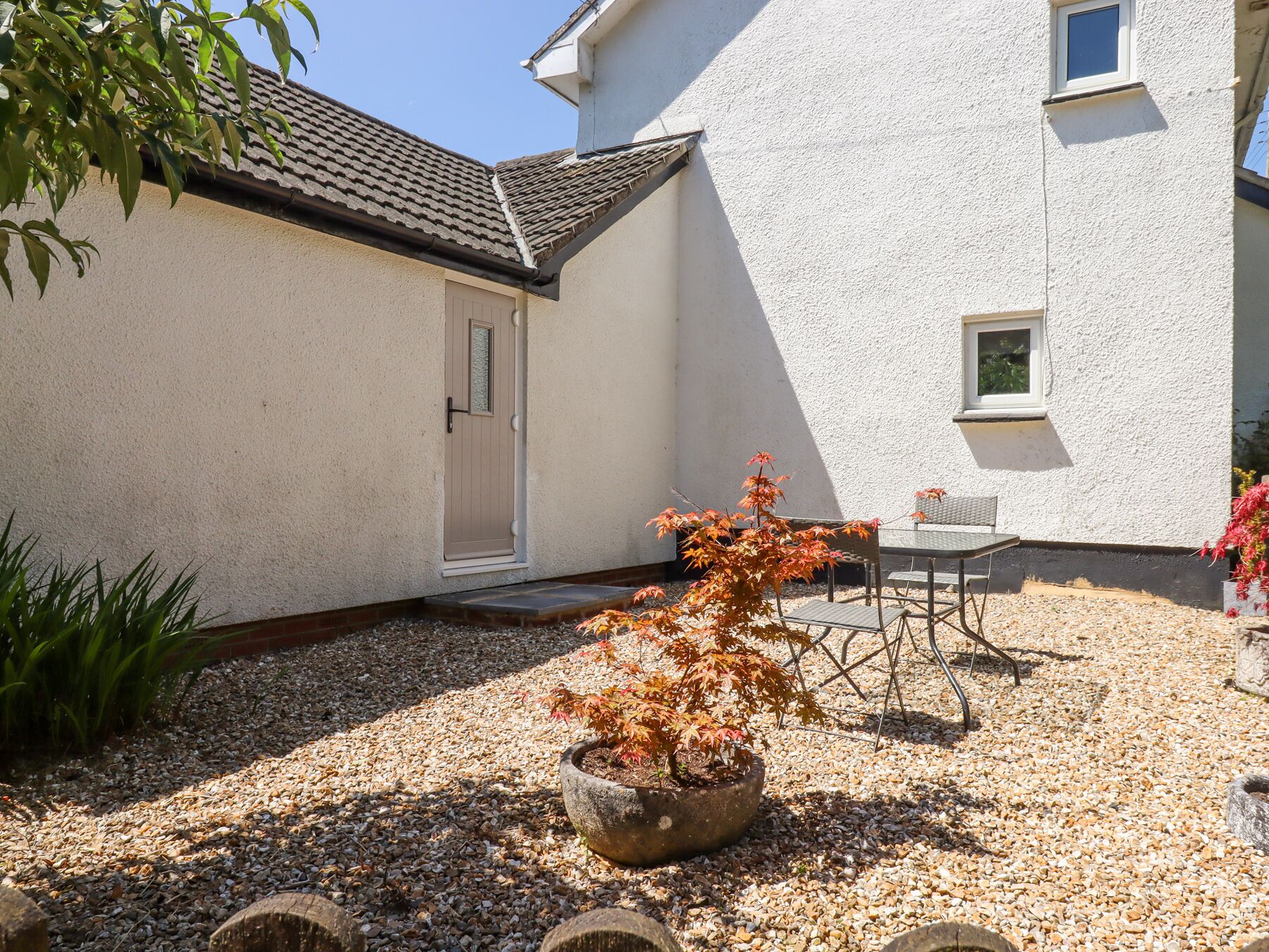 A house with a tiled roof, a white exterior, a door, a window, and a small garden area with gravel and a potted plant.