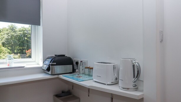 Una pequeña kitchenette con tostadora, hervidor y cafetera sobre una encimera blanca.