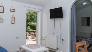 Una habitación con una mesa blanca, un televisor montado en la pared, una cama con ropa de cama estampada y un reloj en la pared.