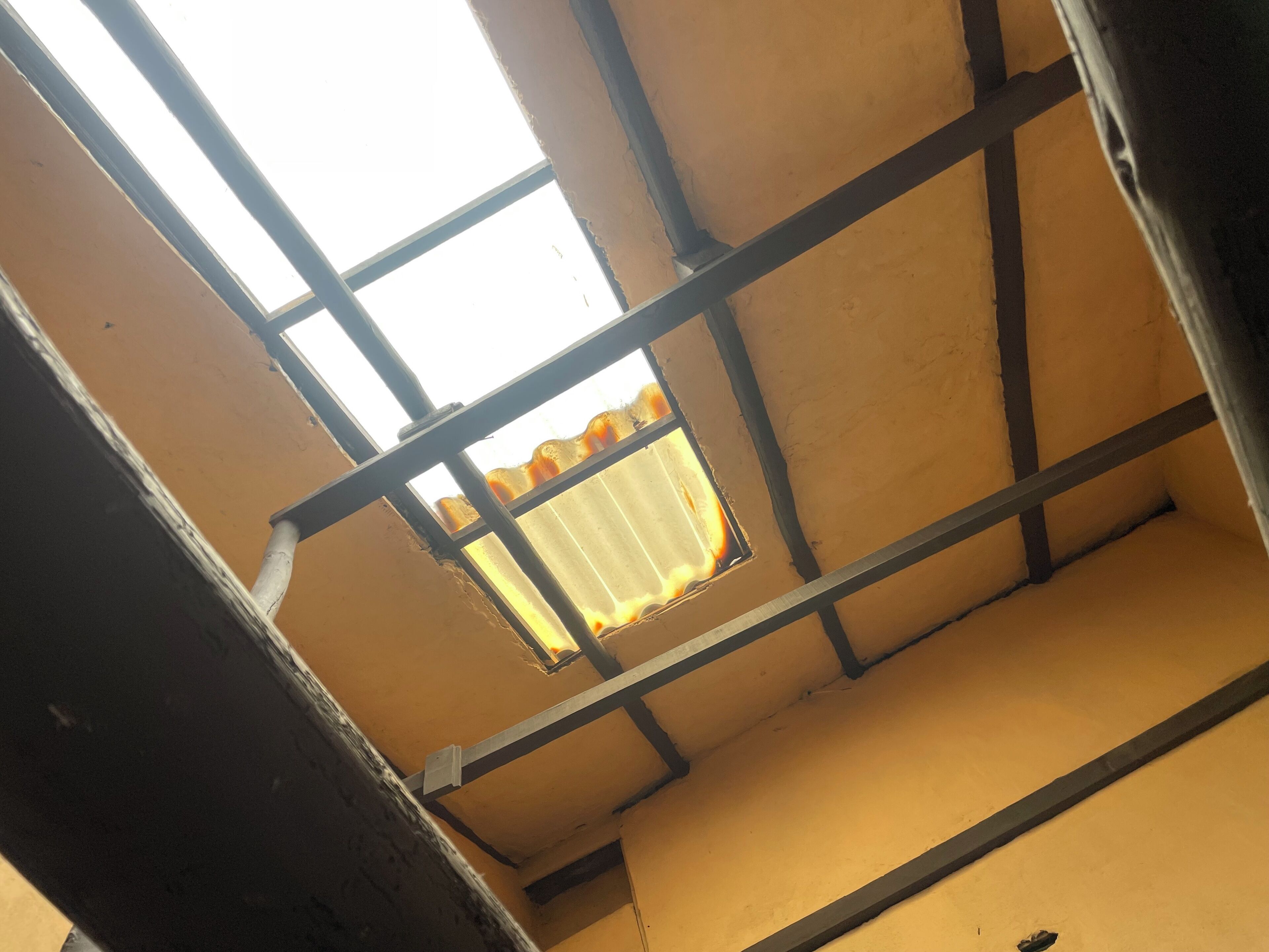A room with a high ceiling, exposed beams, and a window with a corrugated metal exterior.