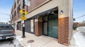 A building with a brick facade, a storefront with glass doors, and a sidewalk with snow. - Cozy Condo, Sleeps 2! (Chicago)
