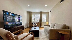 En stue med et fladskærms-tv, en sofa, en lænestol, et sofabord og et spiseområde med stole og et bord.