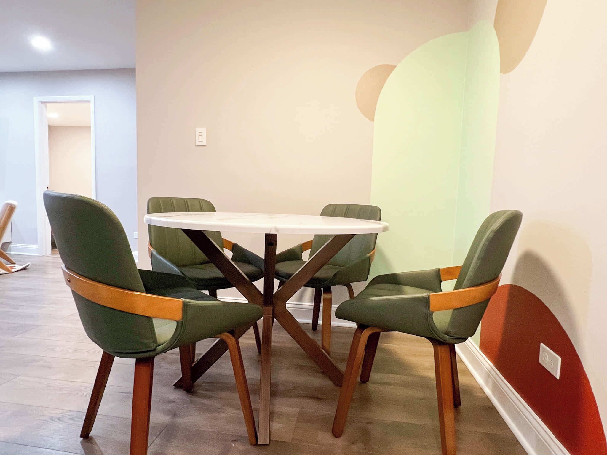 A dining area with a round table and six chairs with wooden frames and green upholstery.