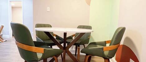 A dining area with a round table and six chairs with wooden frames and green upholstery.