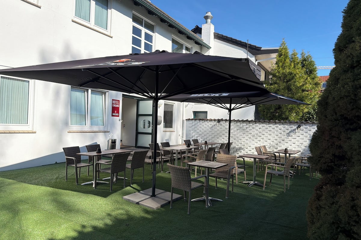 Un espace extérieur aménagé avec des tables et des chaises, un grand parasol et un panneau indiquant les services offerts par l’hôtel.