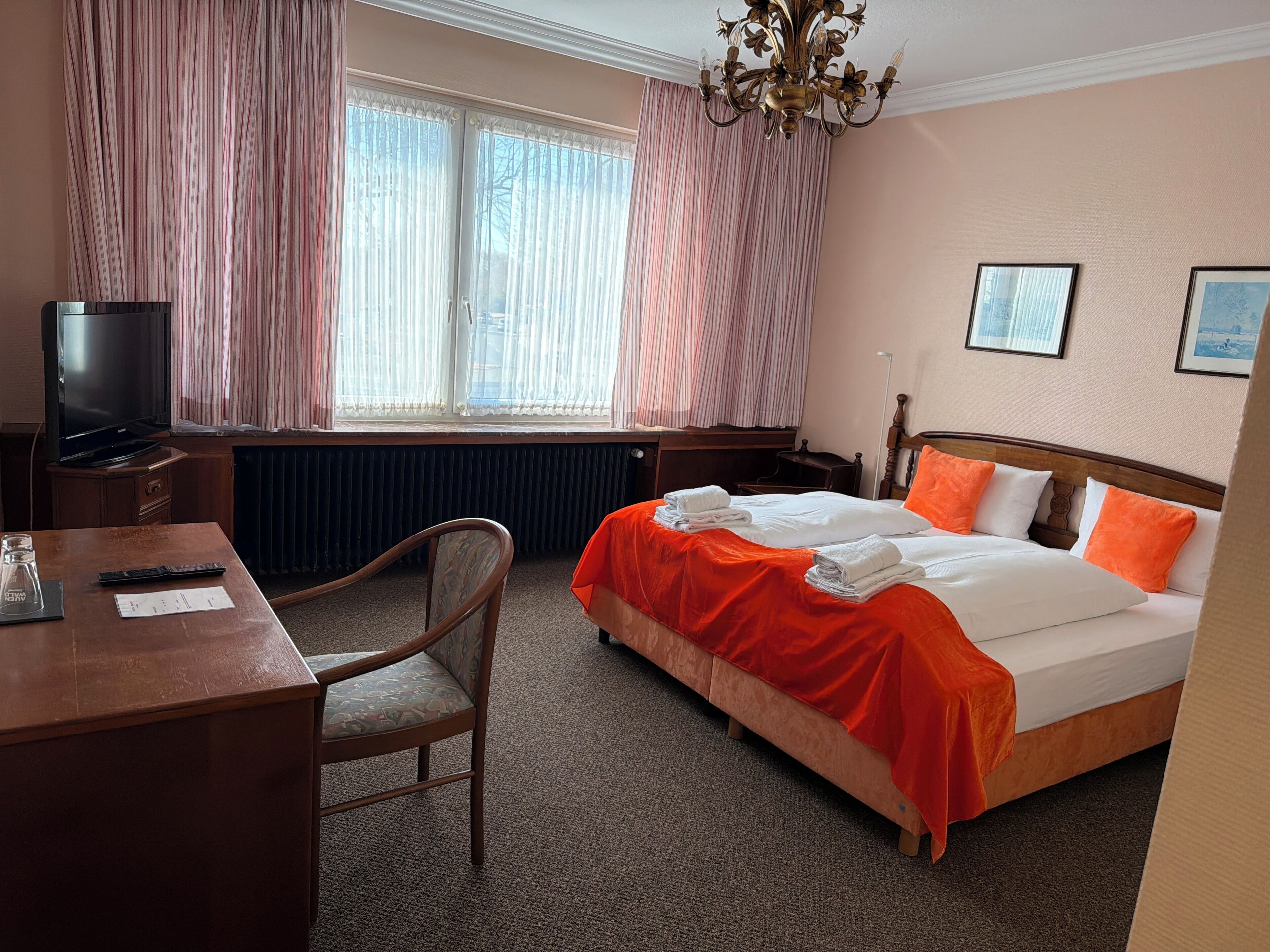 A hotel room with a bed, a desk, a chair, a television, and a window with curtains.