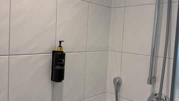 A shower area with white tiles, a handheld showerhead, and a bottle of shampoo.