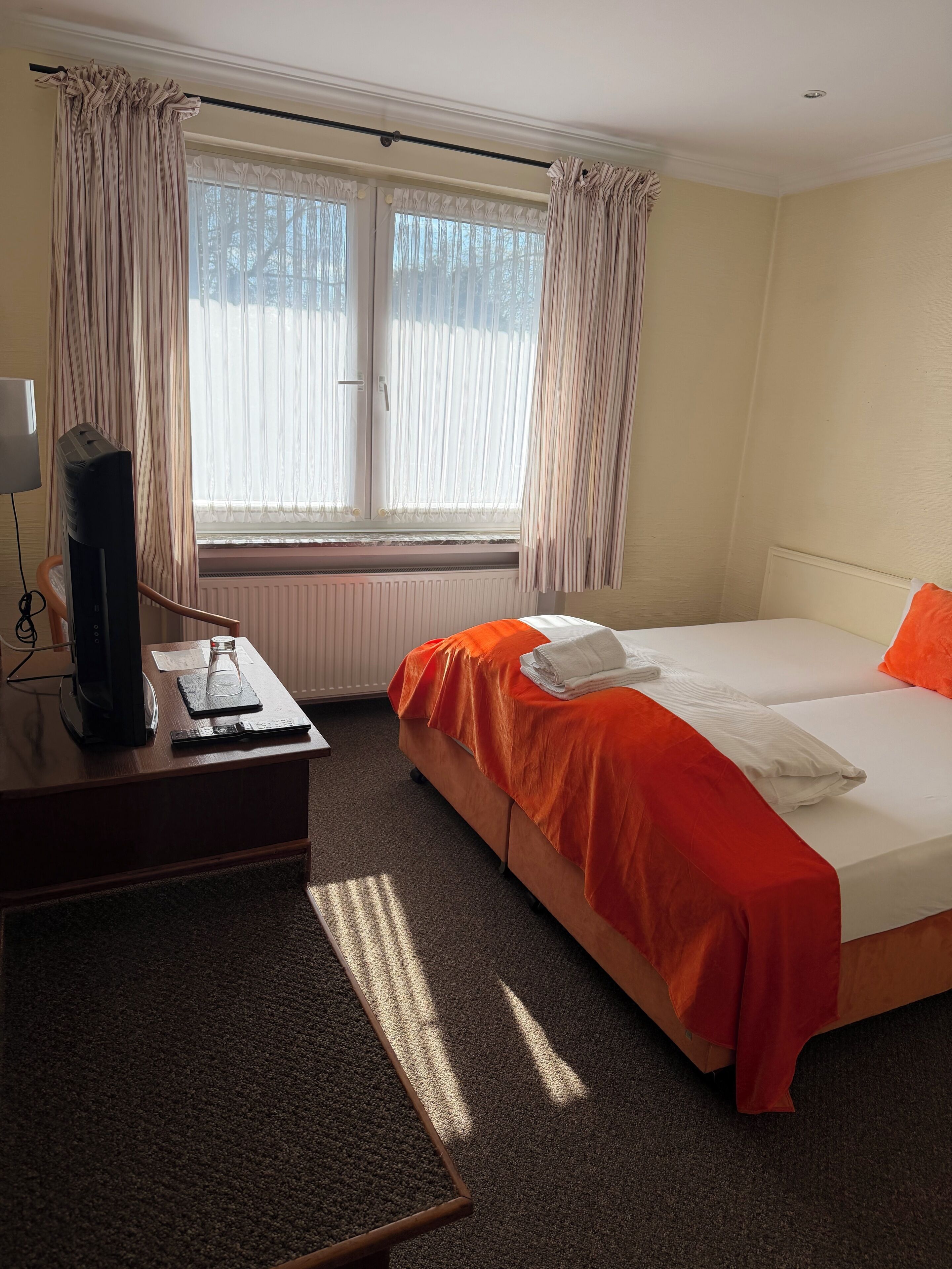 A hotel room with a bed, a desk, a television, and a window with curtains.