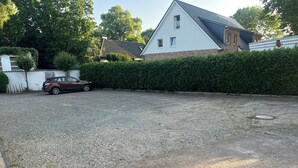 Un camino de entrada residencial con un automóvil estacionado, un seto y una casa con techo inclinado.