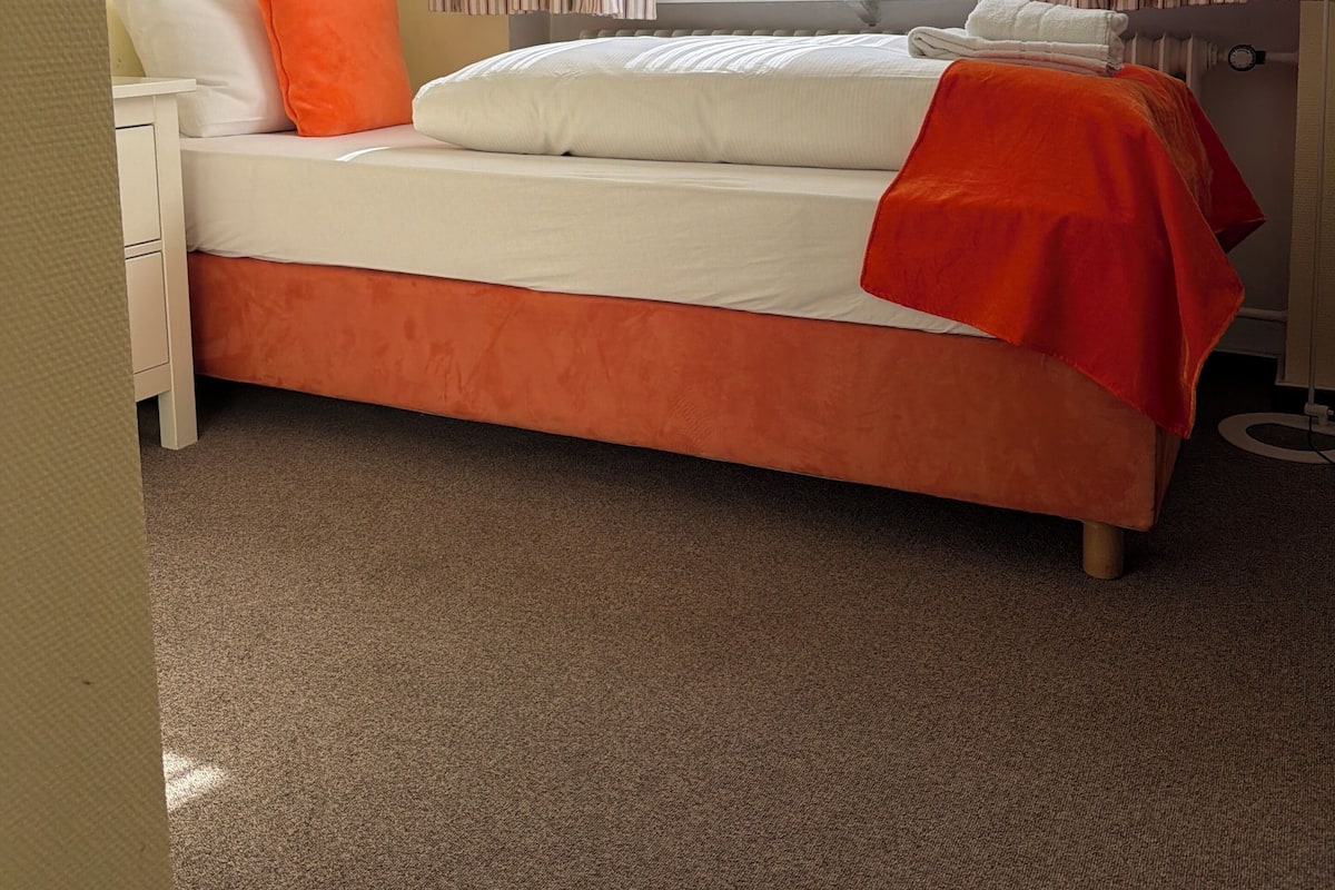 Une chambre à coucher comprenant un lit, une table de chevet, une commode et une fenêtre avec des rideaux.
