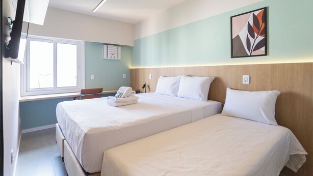 Une chambre d’hôtel avec deux lits, une fenêtre, un téléviseur à écran plat et une œuvre d’art accrochée au mur.