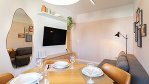 Un coin repas avec une table en bois dressée pour quatre personnes, un téléviseur fixé au mur et un canapé à l’arrière-plan.
