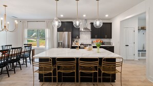 Una cocina moderna con una isla central, luces colgantes y una zona de comedor con sillas.