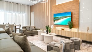 A modern living room with a large flat-screen TV, a wooden accent wall, and a view of a beach. - 4001SB Sonoma (Kissimmee)