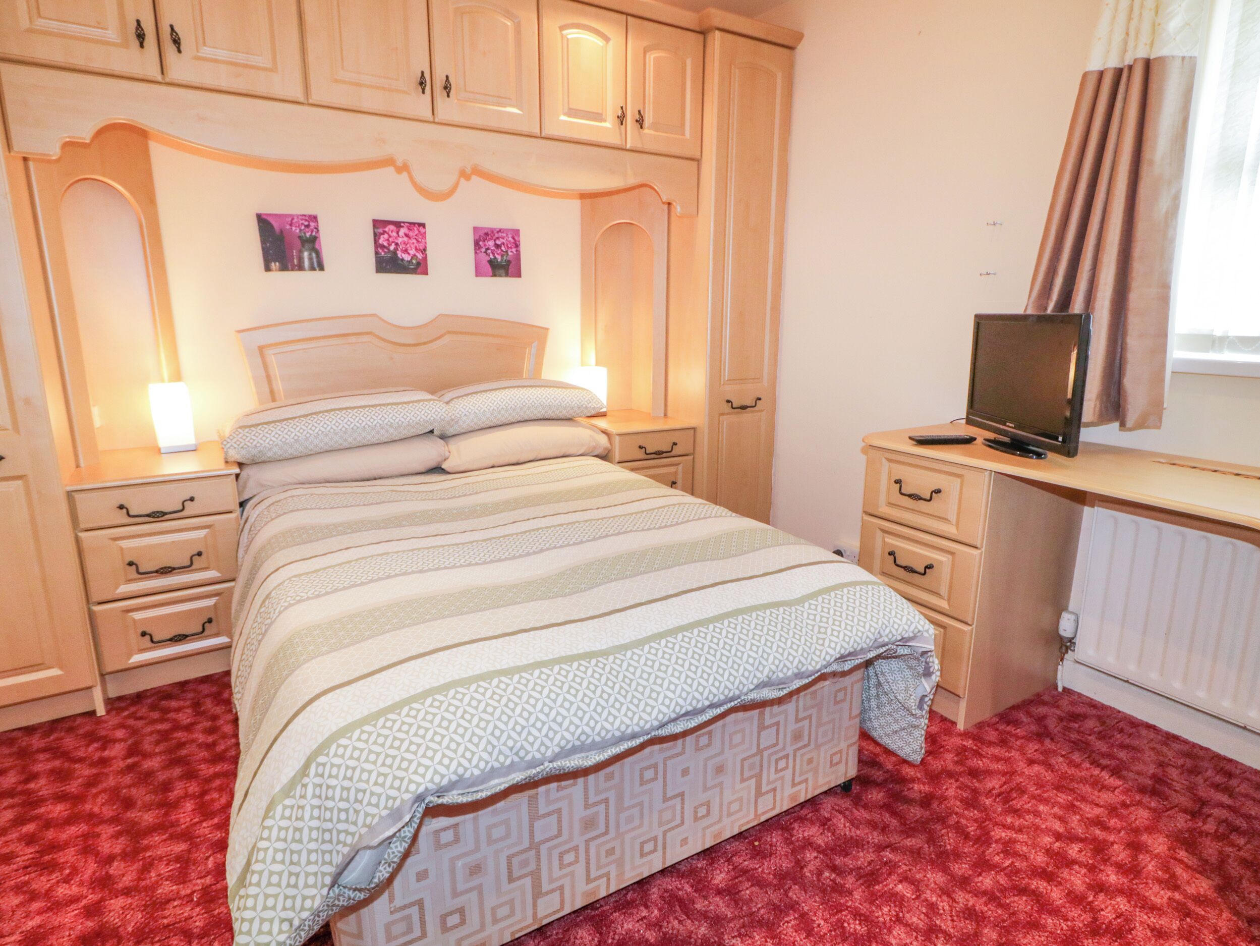 A bedroom with a bed, bedside tables, a desk with a computer, and a radiator.
