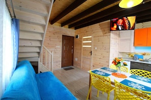 A wooden interior with a staircase, a dining area with yellow chairs, and a television mounted on the wall.