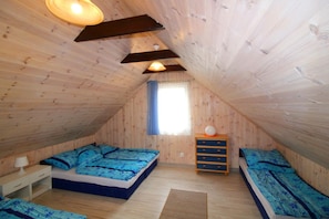 A bedroom with a sloped ceiling, wooden walls, a bed with blue bedding, a bedside table, and a dresser.