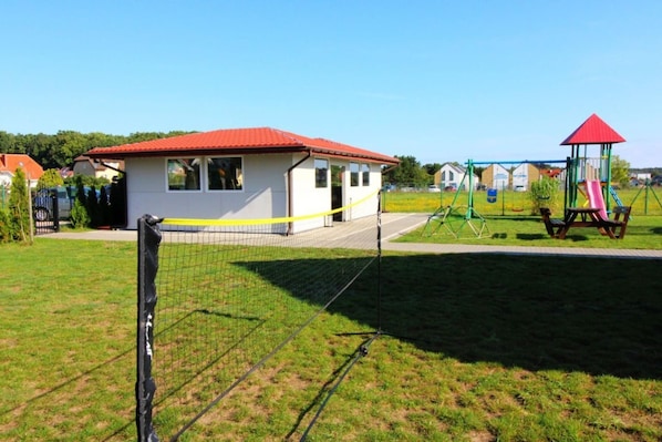 A fenced sports field with a small building, a playground, and a red-roofed structure.
