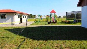 Een omheind buitenterrein met een schommel, glijbaan en klimrek.