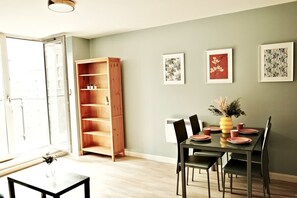 A dining area with a table set for four, a wooden bookshelf, and framed artwork on the wall.