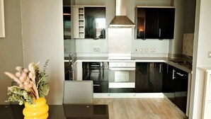 A modern kitchen with black cabinets, stainless steel appliances, and a central range hood. - Central 2BR Birmingham Apt - Free Parking (Birmingham)