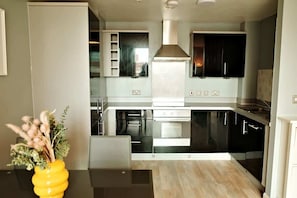 Una cocina moderna con armarios negros, electrodomésticos de acero inoxidable y una campana extractora central.