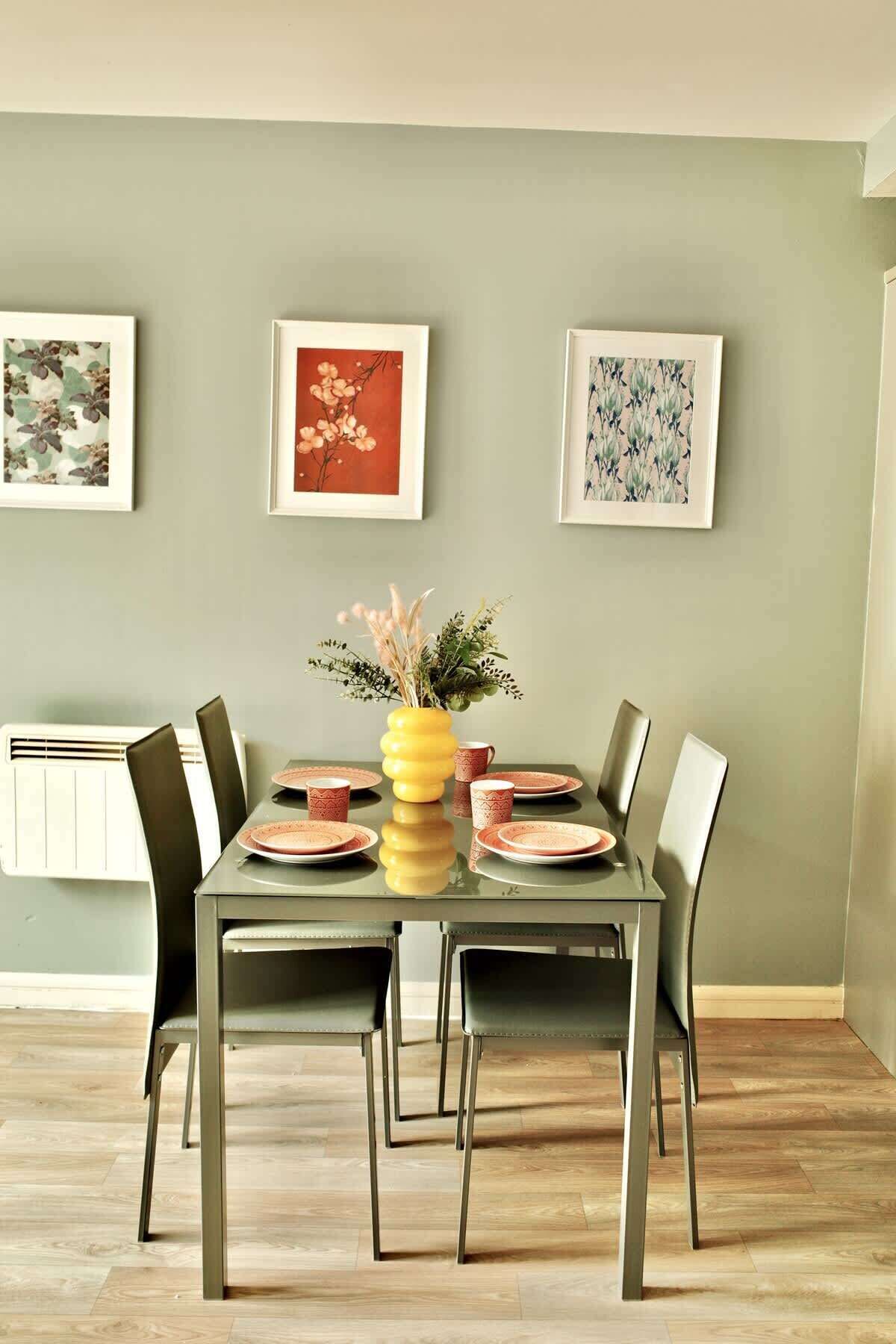 Een eetgedeelte met een tafel voor vier personen, omringd door stoelen, met ingelijste kunstwerken aan de muur.