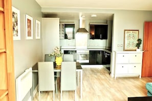 Una cocina moderna con armarios blancos, un comedor con mesa y sillas, y una sala de estar con sofá.