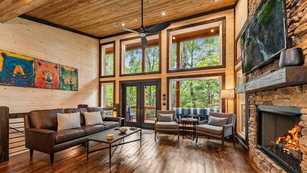A spacious living room with a fireplace, large windows, and a ceiling fan. - Olivers Modern Twist- Cherry Log GA (Cherry Log)