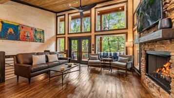A spacious living room with a fireplace, large windows, and a ceiling fan.