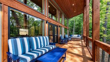 A covered deck with wooden flooring, blue and white striped sofas, and chairs.