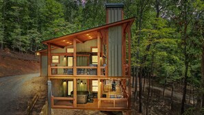 A two-story wooden cabin with multiple windows and a balcony, surrounded by a forest. - Olivers Modern Twist- Cherry Log GA (Cherry Log)
