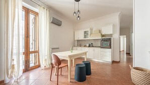 A modern kitchen with white cabinets, a tiled backsplash, and a built-in oven. There is a dining table with two chairs and a small stool. - Gorizia Apartment by Wonderful Italy (Palermo)