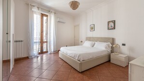 A bedroom with a large bed, a bedside table with a lamp, a window with curtains, and a door. - Gorizia Apartment by Wonderful Italy (Palermo)