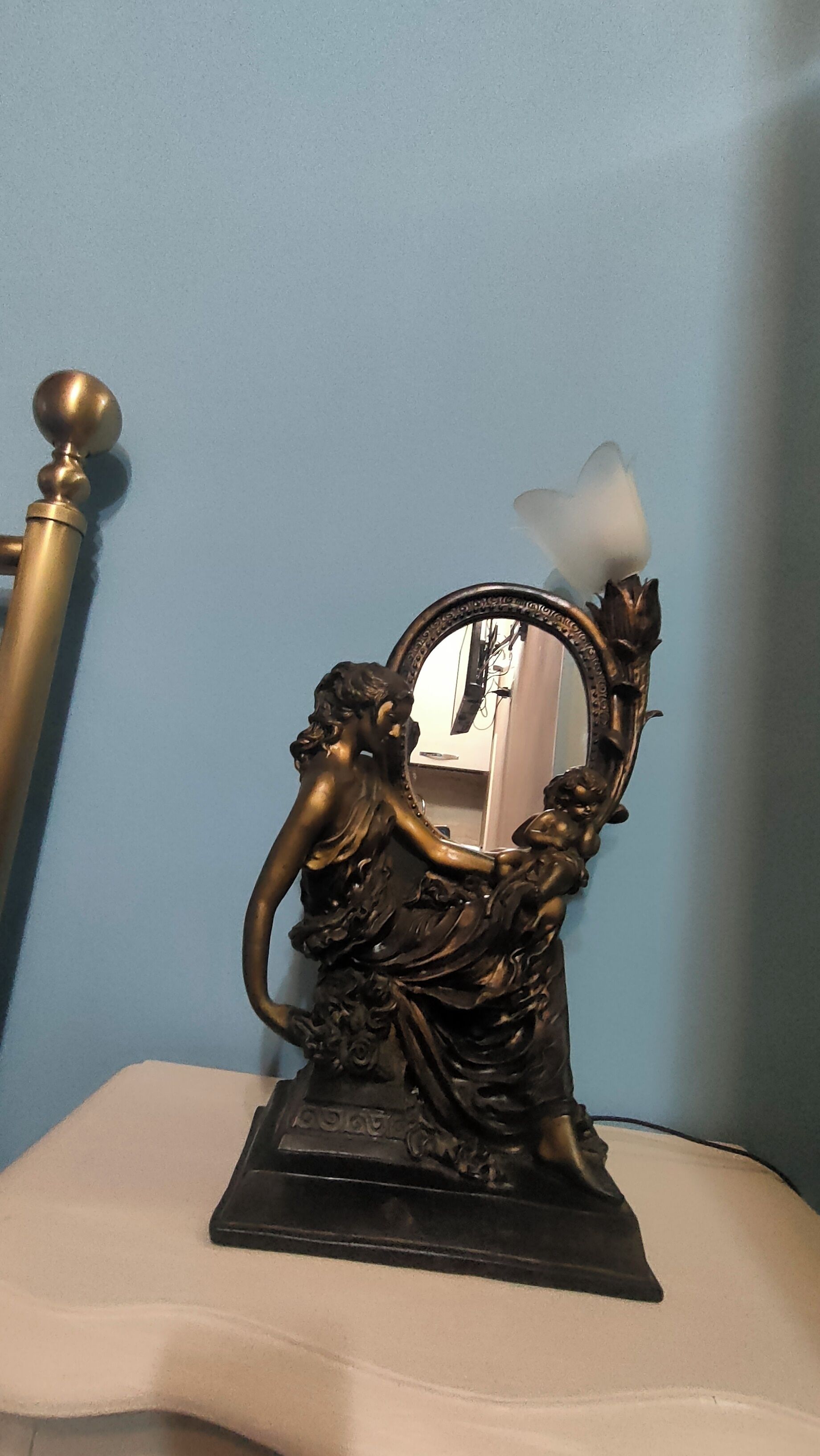 A bronze statue of a woman holding a mirror with a decorative base.