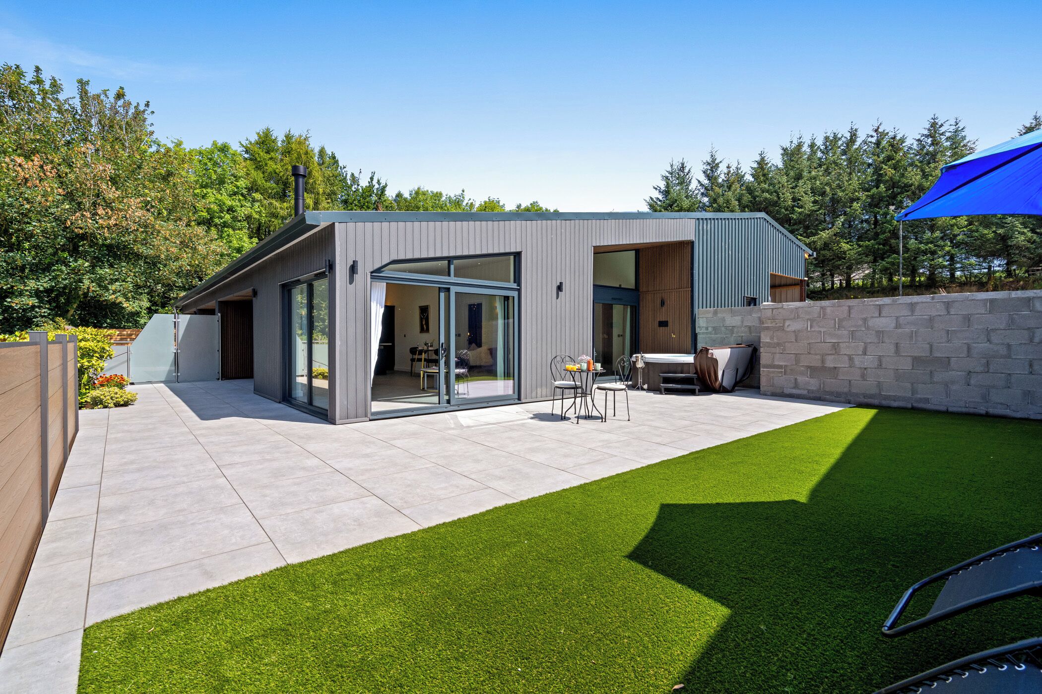 Une maison moderne dotée d’un patio, d’une entrée avec porte vitrée et d’un petit espace extérieur aménagé pour s’asseoir.
