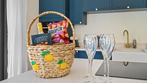 Una cocina con una cesta de mimbre llena de aperitivos y una botella, dos copas de vino vacías sobre la encimera y armarios azules al fondo.