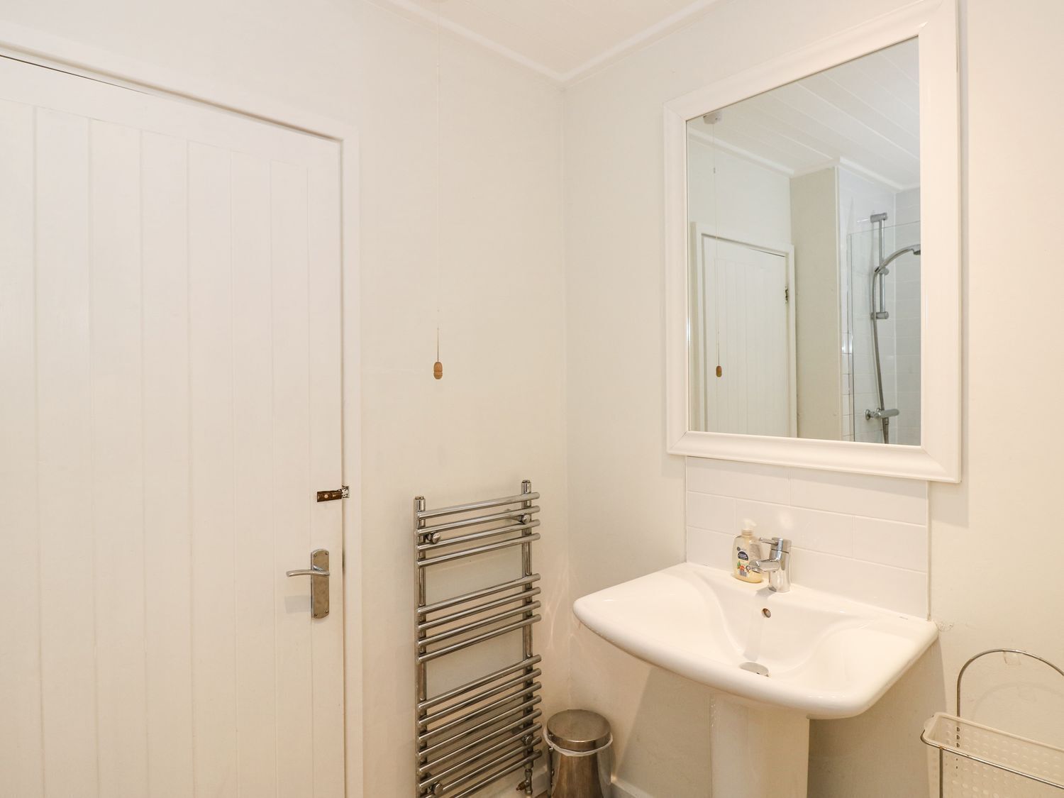 Een kleine, schone badkamer met een witte wastafel, een spiegel en een handdoekhouder.