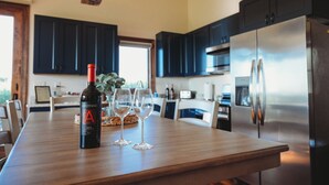 Une cuisine moderne avec des meubles de couleur sombre, un réfrigérateur en acier inoxydable et une table à manger en bois sur laquelle se trouvent une bouteille et des verres.