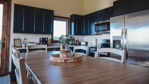 Une cuisine moderne avec des meubles de couleur sombre, des appareils en acier inoxydable et une table à manger en bois, accompagnée de chaises.