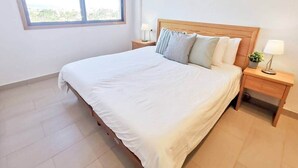 Un dormitorio con una cama grande, dos mesitas de noche, un ventanal y vistas al verdor exterior.