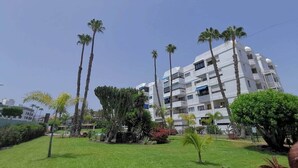 Un hotel de varios pisos con fachada blanca, rodeado de césped cuidado y palmeras.