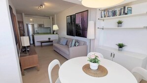 Una sala moderna con una mesa de comedor blanca, un sofá y una cocina al fondo.