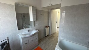 Un baño moderno con lavamanos, espejo y bañera blancos.